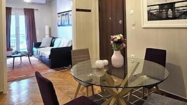 Uma sala de jantar com mesa e cadeiras de vidro, um vaso com flores e uma porta com um quadro emoldurado.