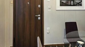 Quarto com porta de madeira, quadro na parede, uma cadeira e uma mesa.