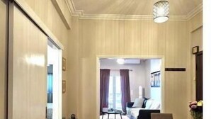 Quarto de hotel com área de jantar, mesa de vidro e cadeiras, piso de madeira em padrão herringbone e luminária no teto.