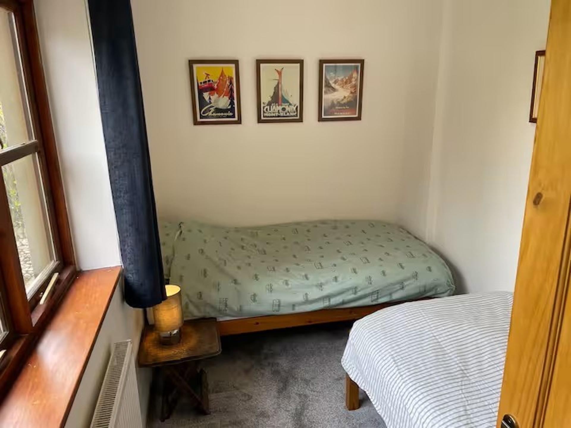 A bedroom with a bed, a small table with a lamp, and three framed pictures on the wall.