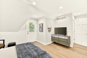 Une chambre à coucher avec un lit, une commode, un téléviseur et une porte.