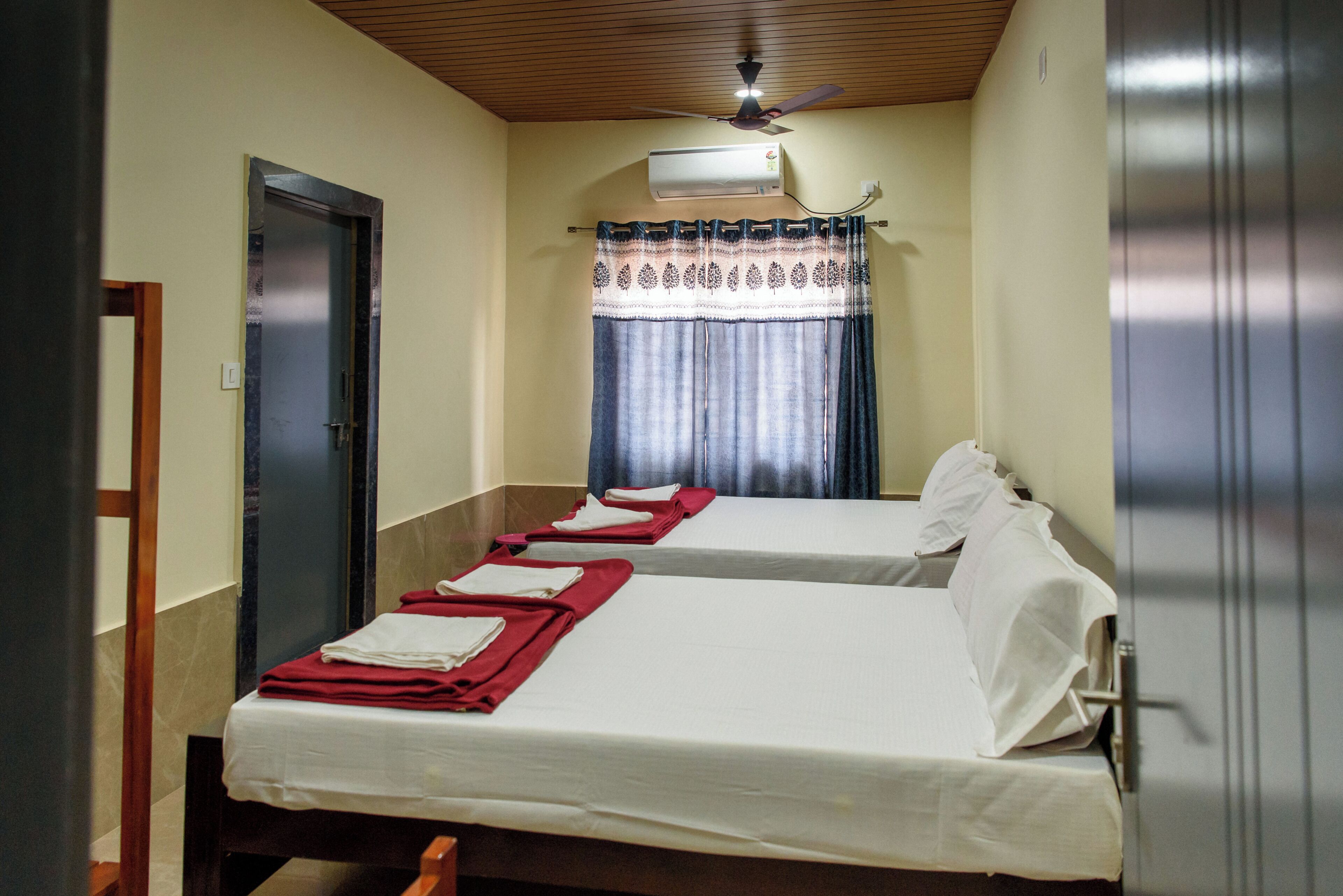 A room with two beds, a ceiling fan, an air conditioning unit, and a door.