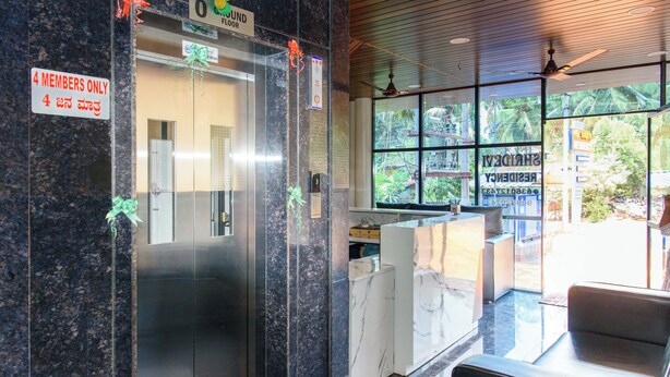 Zona de recepción de un hotel con suelo de mármol, mostrador de recepción y un ascensor de cristal.