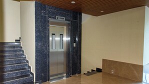 Un ascensor moderno con pared de mármol, una escalera y un cartel que indica '2do Piso'.