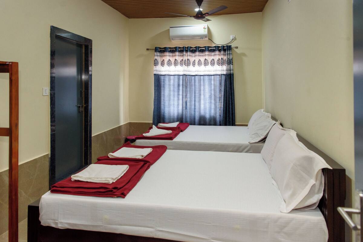 A hotel room with two beds, a ceiling fan, an air conditioning unit, and a curtain.