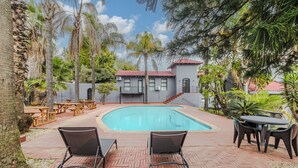 A swimming pool with lounge chairs and tables, surrounded by palm trees and a building with a red roof. - Boutique Hotel-Style Room In Ferndale-B2 (Randburg)
