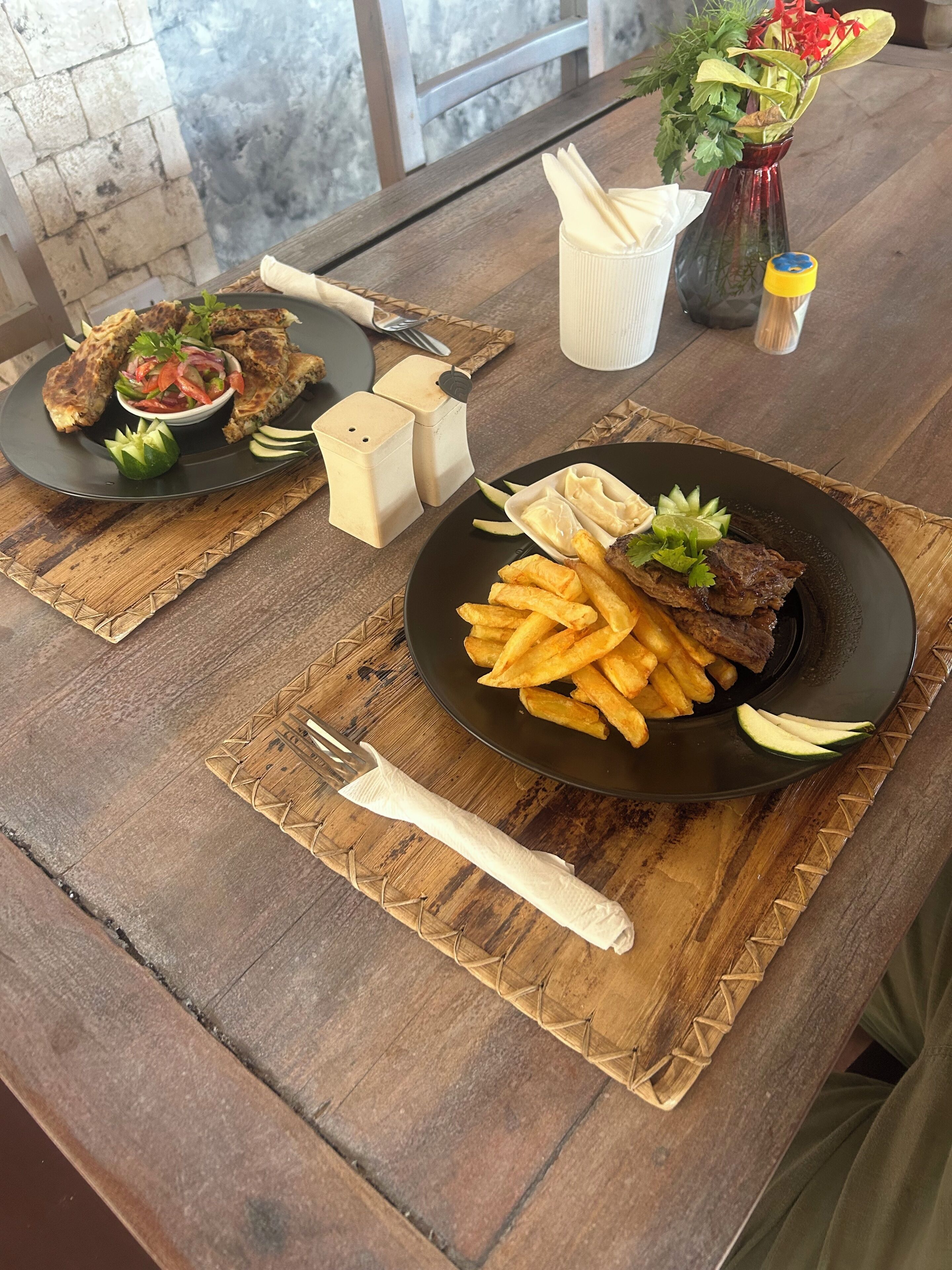 A wooden table with two plates of food, a salt and pepper shaker, and a vase with flowers.