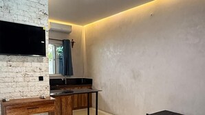 A modern living room with a sofa, a coffee table, a TV mounted on a brick wall, and a ceiling fan. - King Simba Hotel & Restaurant (Bwejuu)