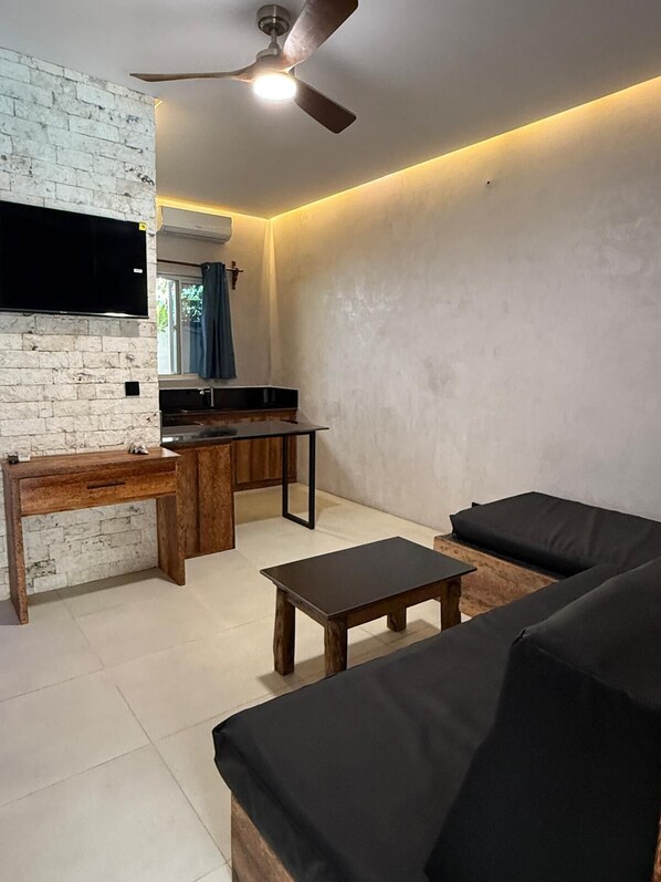 Ein modernes Wohnzimmer mit einer Couch, einem Couchtisch, einem an einer Ziegelwand montierten Fernseher und einem Deckenventilator.