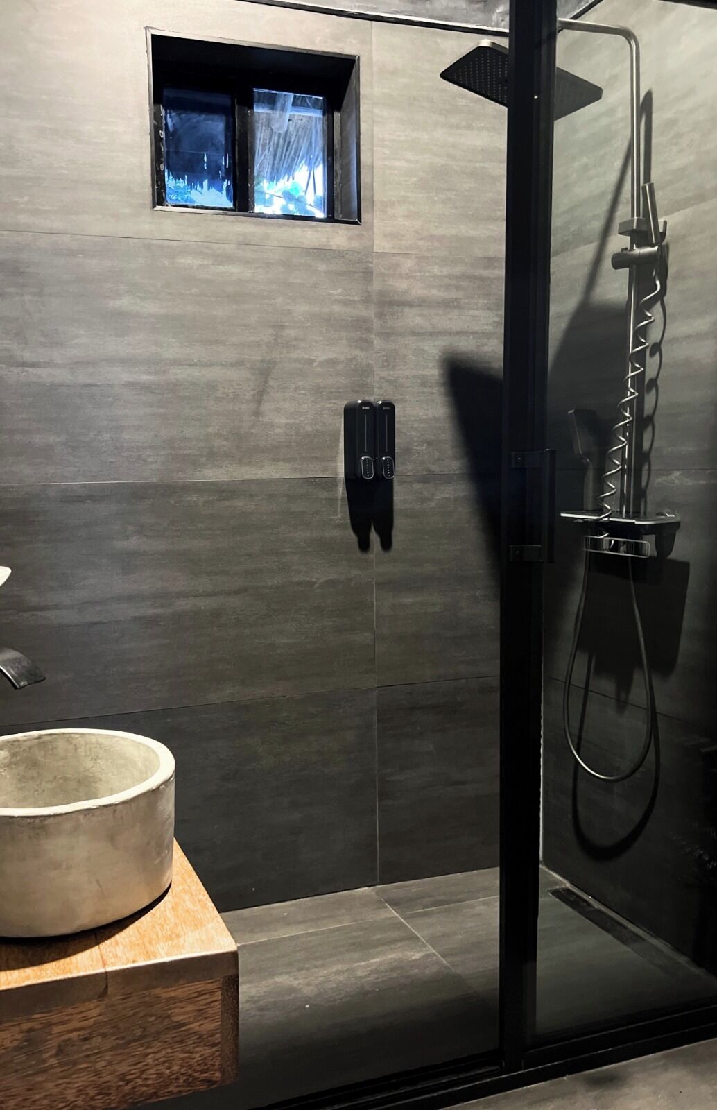 A modern bathroom with a glass-enclosed shower, a built-in sink, and a small window.