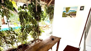 A wooden bench under a thatched roof, a white wall with a picture, and a green cushion. - King Simba Hotel & Restaurant (Bwejuu)