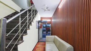 A staircase with metal railings, a ceiling fan, a patterned carpet, and a sofa against a wooden wall. - Hotel Royal Residency (New Delhi)