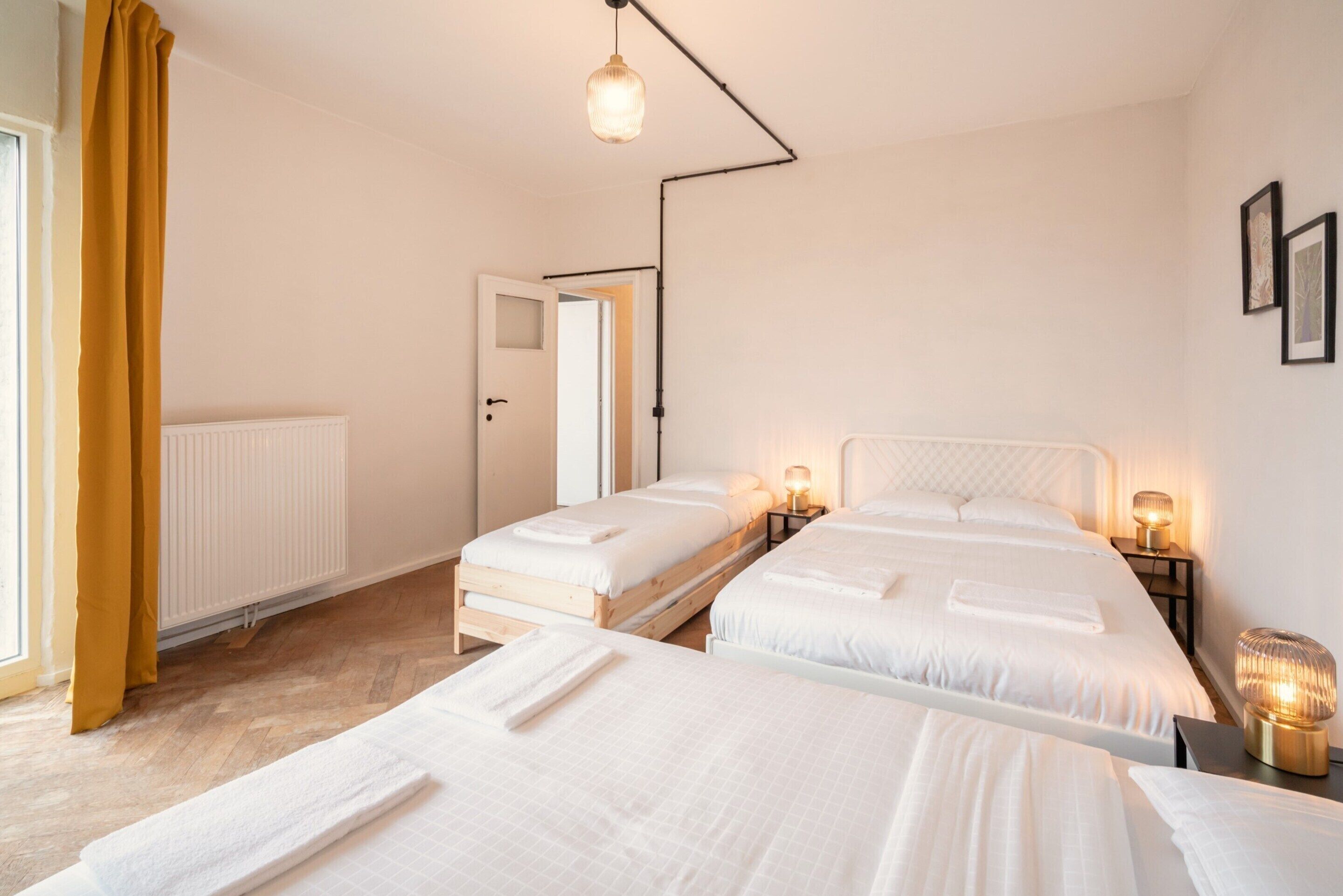 A hotel room with two beds, a radiator, a door, and a wall-mounted light fixture.