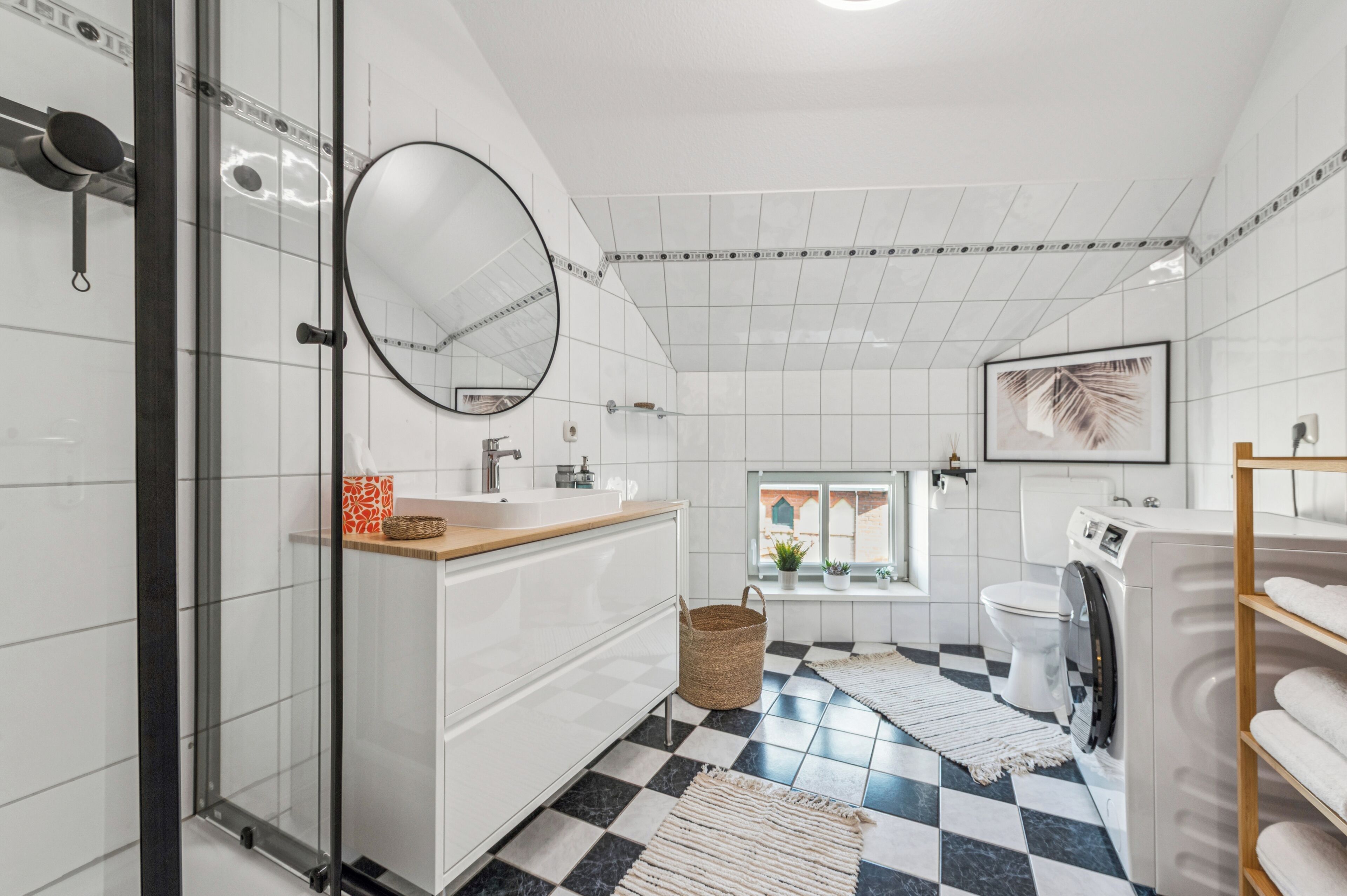 Une salle de bain moderne avec un carrelage à motifs géométriques, un grand miroir, un lavabo, des toilettes et un lave-linge.