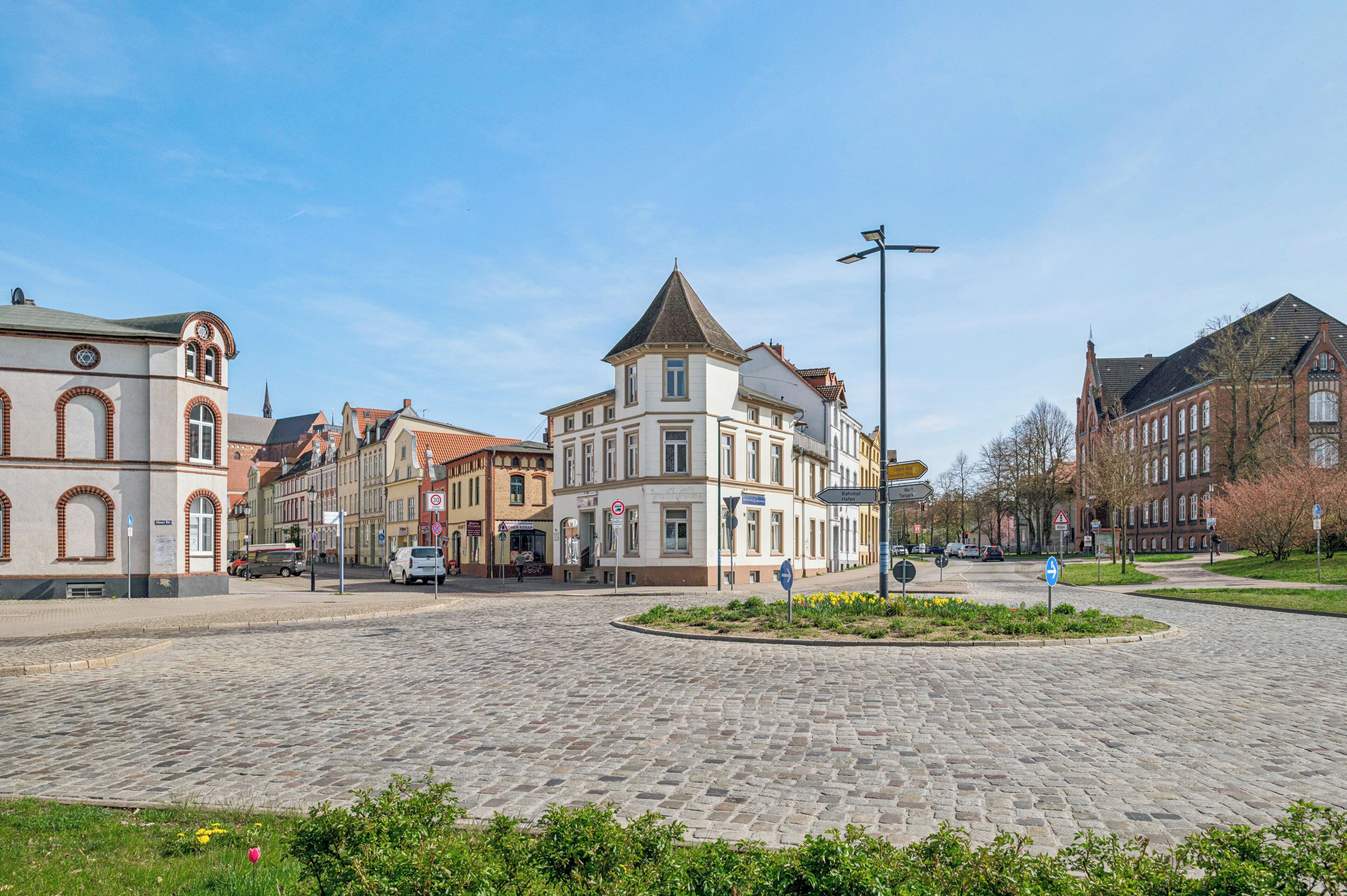 Une rue pavée bordée de bâtiments historiques, un carrefour giratoire et un ciel dégagé.