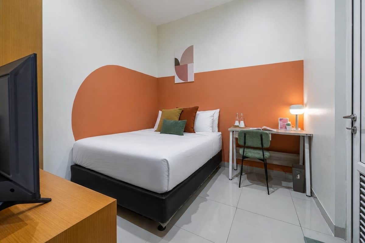 Una habitación de hotel con cama, escritorio con lámpara, televisor y puerta.