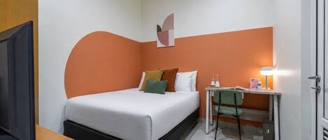 Una habitación de hotel con cama, escritorio con lámpara, televisor y puerta.