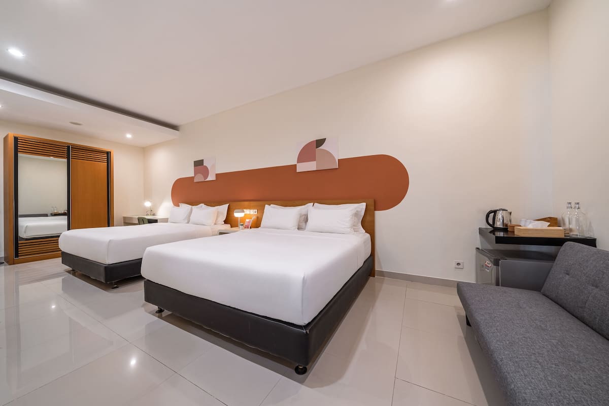 Habitación de hotel con dos camas, un sofá, un escritorio con lámpara, un espejo y una obra de arte en la pared.