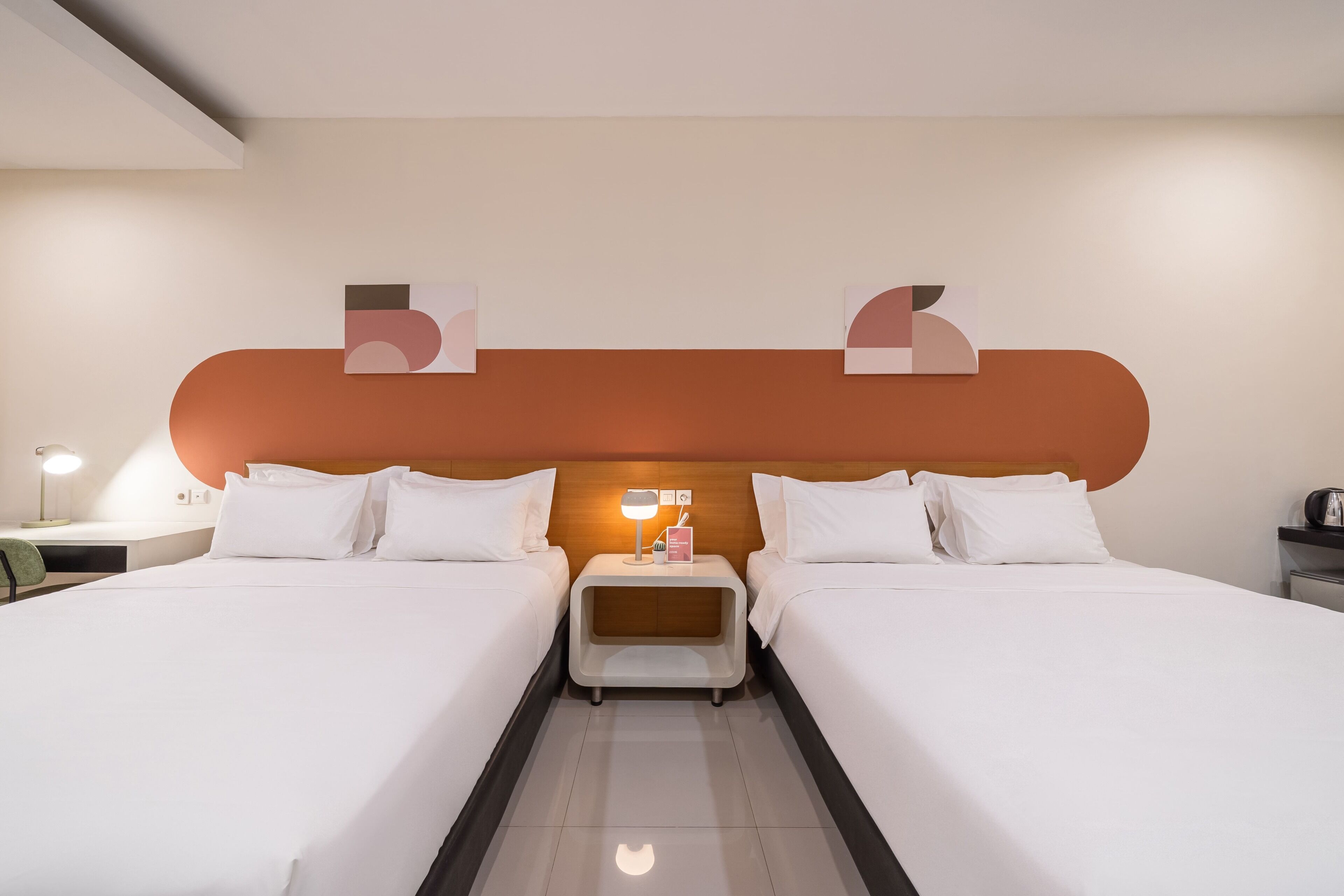 A hotel room with two beds, a nightstand with a lamp, and a wooden headboard.