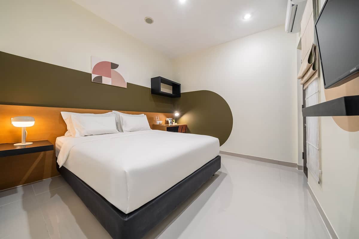 Una habitación de hotel moderna con una cama grande, mesita de noche, lámpara y televisor.