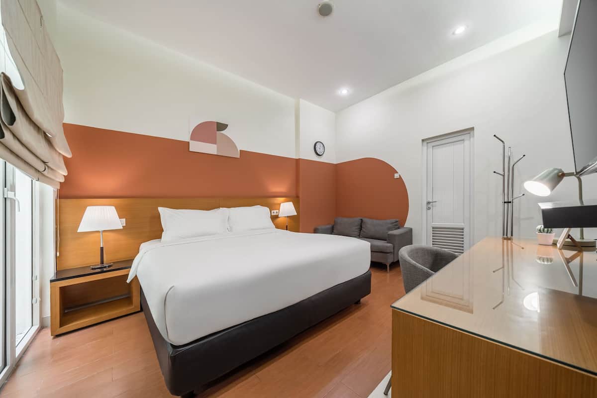 Una habitación de hotel moderna con una cama grande, un escritorio con lámpara, un sofá, un reloj y una puerta.