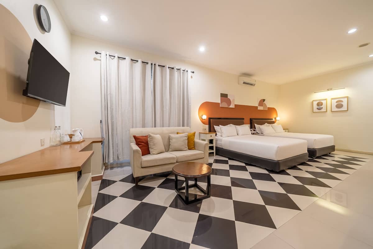 Habitación de hotel con piso a cuadros, un sofá, una cama, un televisor y una mesita de centro.