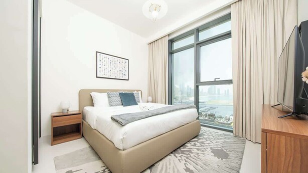 Habitación de hotel moderna con una cama grande, una mesita de noche, un televisor y vistas de la ciudad.