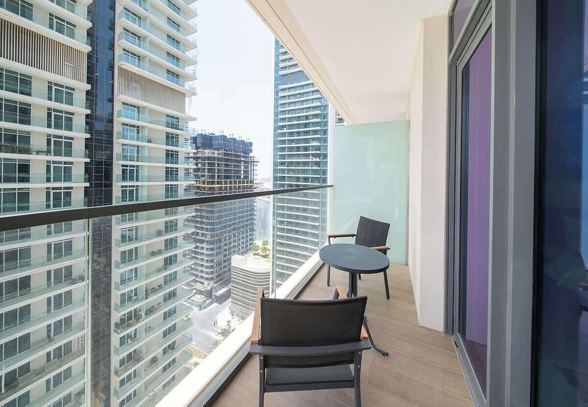 Un balcon doté d’une rambarde en verre, de deux chaises et offrant une vue sur les immeubles de grande hauteur.