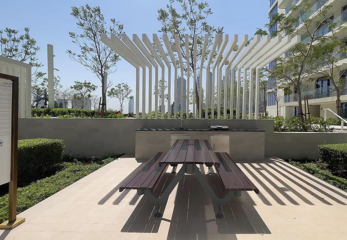 Un espace extérieur moderne aménagé avec des sièges et une table de pique-nique, entouré de verdure et bordé d’une structure blanche.