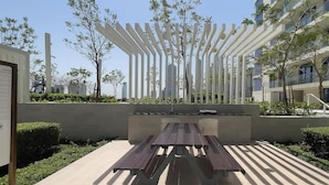 Un espacio al aire libre moderno con una mesa de picnic, rodeado de follaje y una estructura blanca.