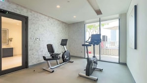 Un gimnasio moderno con dos bicicletas estáticas y una cinta de correr, ventanas amplias y una pared de mármol.