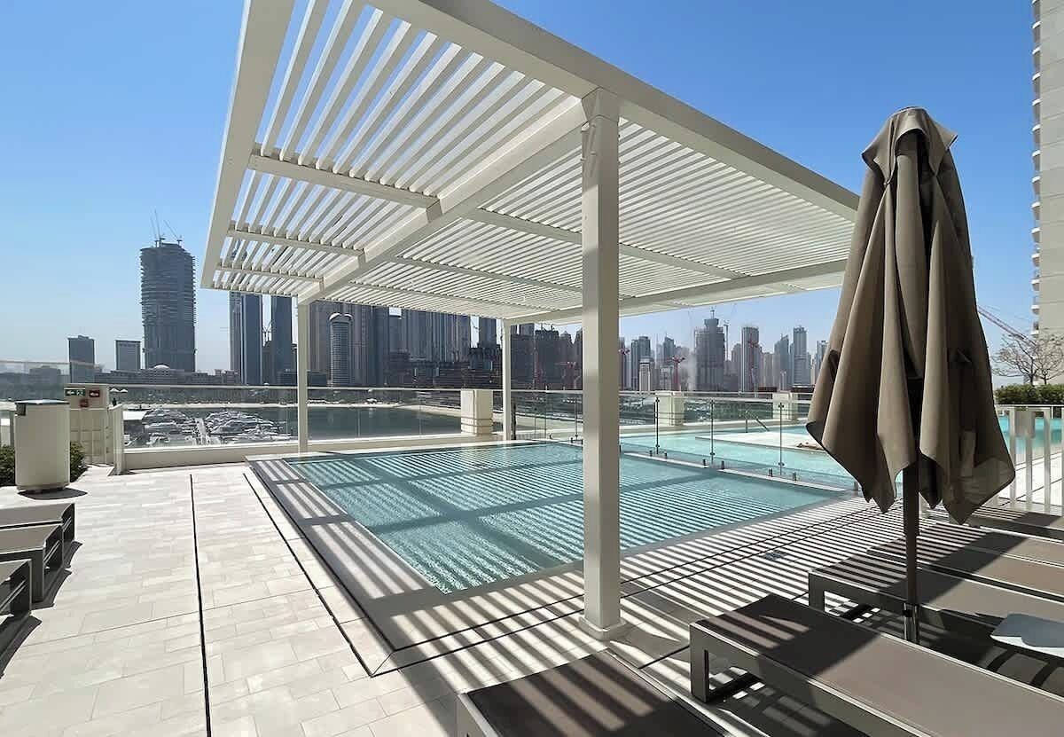 Un espace piscine sur le toit avec vue sur les toits de la ville, un coin salon couvert et un parasol au bord de la piscine.