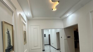 A hallway with white walls, marble flooring, framed artwork, and a modern light fixture.