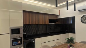 A modern kitchen with a built-in oven, microwave, and washing machine, a wooden dining table, and pendant lighting.