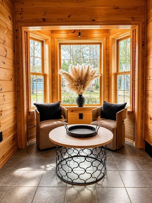 Interior acogedor de una cabaña con paredes de madera, una mesa redonda con sillas y una ventana con vistas a follaje.