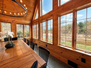 Un intérieur en bois, avec de grandes fenêtres, une table à manger et des chaises.