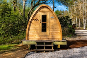 Une cabane en bois avec une porte, des marches menant à l’entrée, et entourée d’arbres.