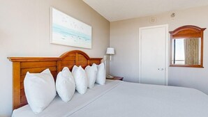 A hotel room with a large bed, a wooden headboard, a painting on the wall, a bedside lamp, and a door with a window. - Oceanfront Balcony | Resort Pools & Lazy River (Myrtle Beach)