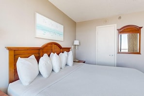 Ein Hotelzimmer mit einem großen Bett, einem Holzkopfteil, einem Gemälde an der Wand, einer Nachttischlampe und einer Tür mit Fenster.