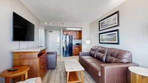A compact living space with a sofa, a TV, a kitchen area, and artwork on the walls. - Oceanfront Balcony | Resort Pools & Lazy River (Myrtle Beach)