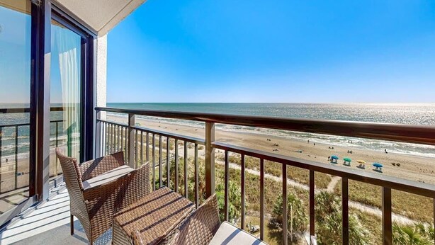 A balcony with wicker furniture overlooking a beach. - Oceanfront Balcony | Resort Pools & Lazy River (Myrtle Beach)