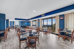 A spacious dining area with multiple tables and chairs, large windows, and a view of the outdoors. - Oceanfront w/2 Queens | Murphy Bed | Lazy River (Myrtle Beach)