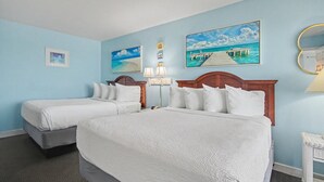 Habitación de hotel con dos camas, una mesita de noche, una lámpara y una obra de arte en la pared que representa una playa.