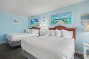 Ein Hotelzimmer mit zwei Betten, einem Nachttisch, einer Lampe und Wandbildern, die eine Strandlandschaft zeigen.