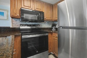 A kitchen with wooden cabinets, a stainless steel refrigerator, a microwave, and an oven. - Oceanfront 1BR Suite + Beach Access + Lazy River (Myrtle Beach)