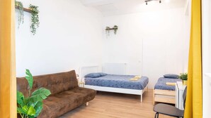 Ein Zimmer mit einem braunen Sofa, zwei Einzelbetten, einem Holztisch und einem Blumentopf.