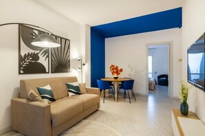 A modern living room with a sofa, a dining table with chairs, a lamp, and a painting on the wall. - Cozy apartment of 60 sqm, ideal for 4 people, located on the ground floor of a building (with some steps at the entrance).The property is located in a residential area, well served and strategically positioned: just 200 mt from Otranto station, convenien (Otranto)