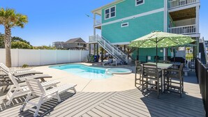 A turquoise two-story building with a swimming pool, deck chairs, and a table with an umbrella. - The Crooked Palm | Luxury Coastal Escape w/ Pool & Views | Steps to the Beach (Oak Island)