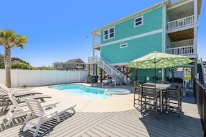 A turquoise two-story building with a swimming pool, deck chairs, and a table with an umbrella. - The Crooked Palm | Luxury Coastal Escape w/ Pool & Views | Steps to the Beach (Oak Island)