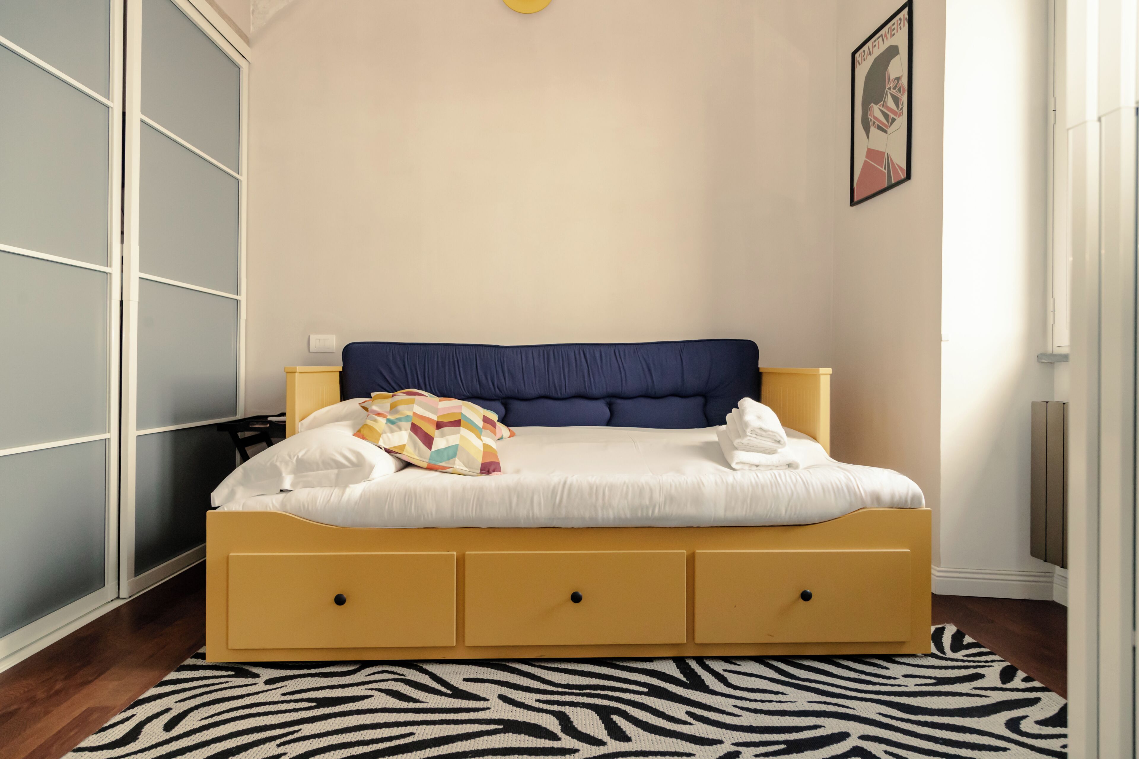 Et soveværelse med en seng, et tæppe med zebraprint, et skab og et billede på væggen.